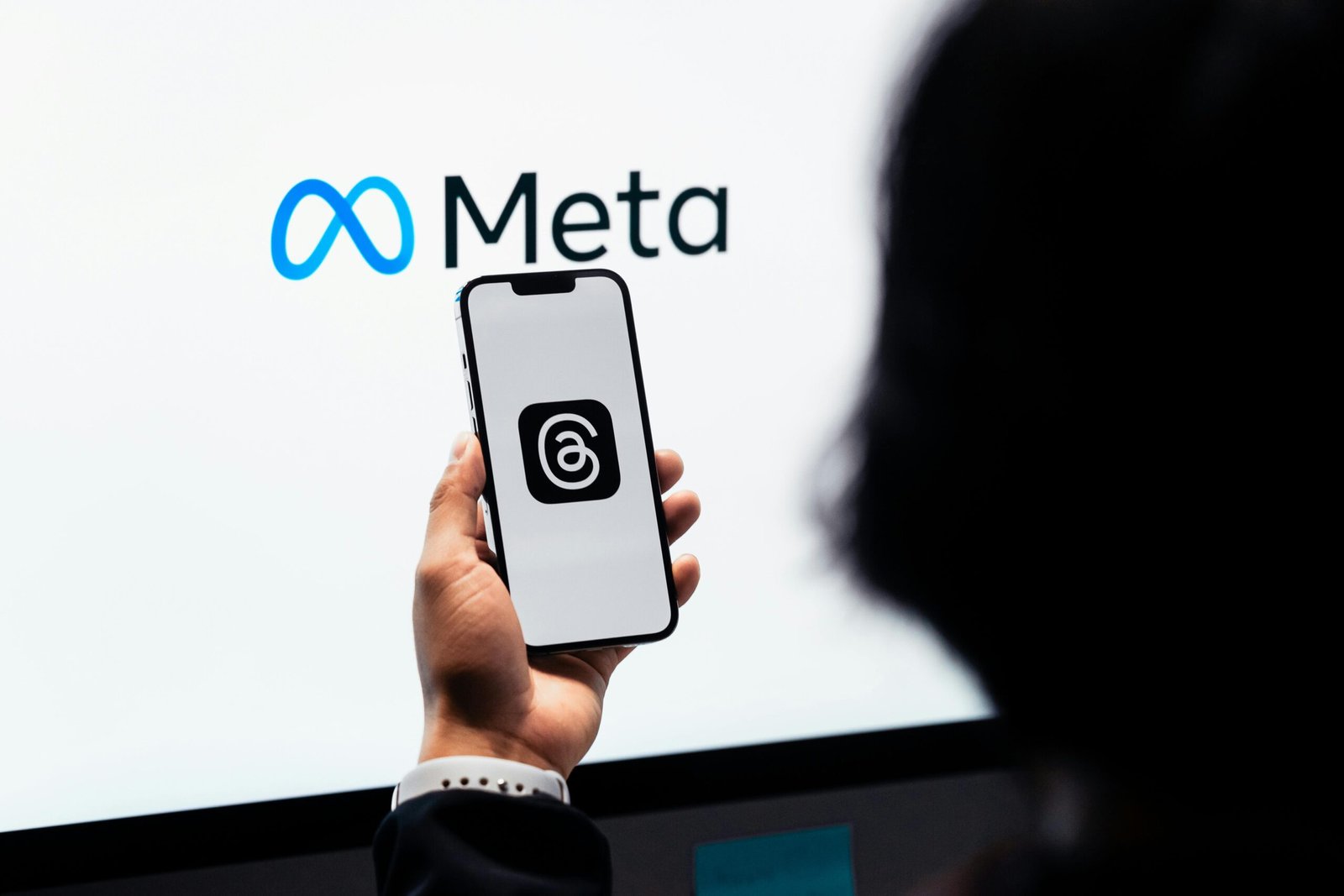 Home Hands holding smartphone with Meta Threads logo on screen, Meta branding in background.